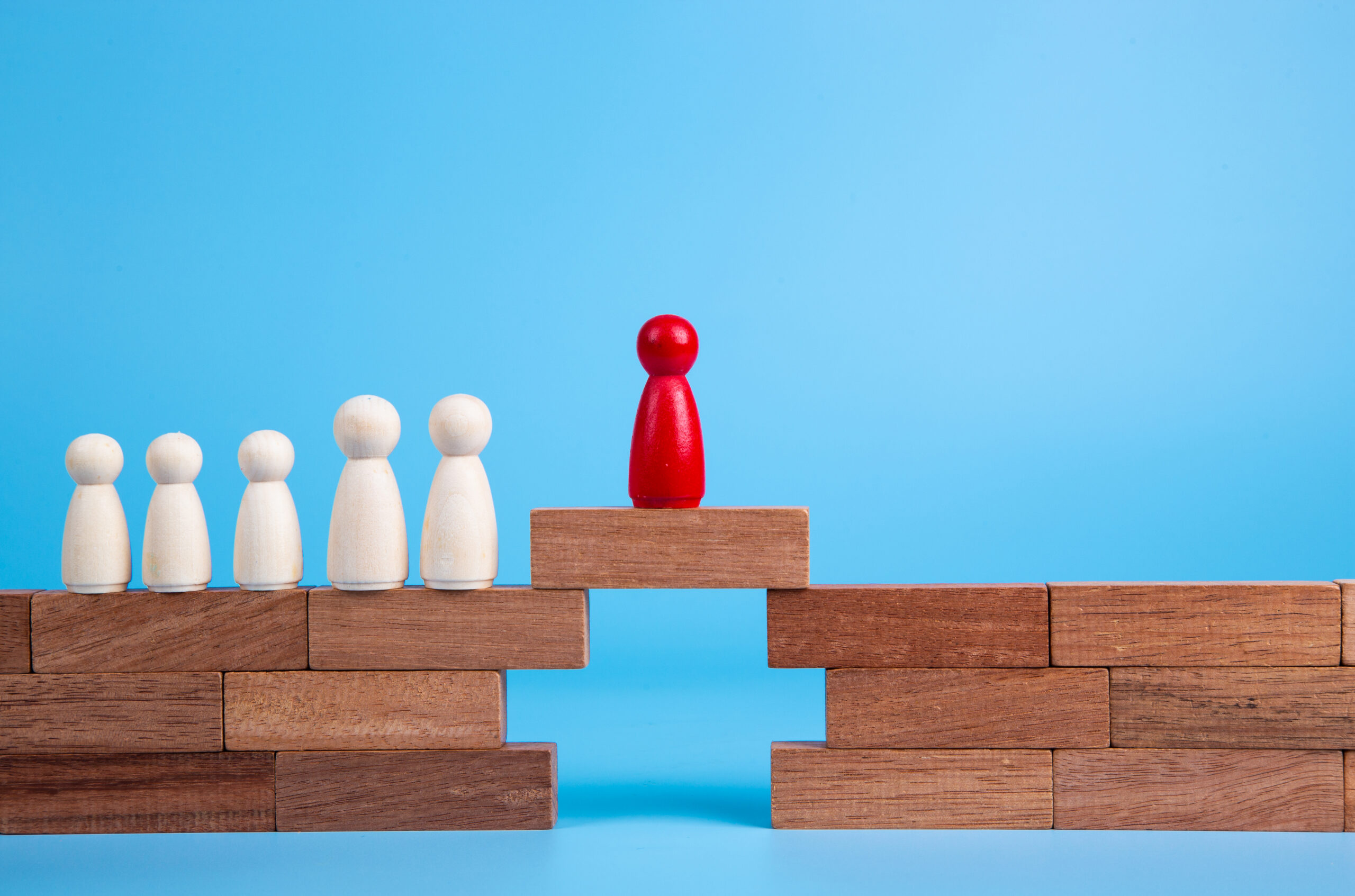 A red pawn crosses a gap on a wooden bridge, while other white pawns waiting, showing strong leadership potential